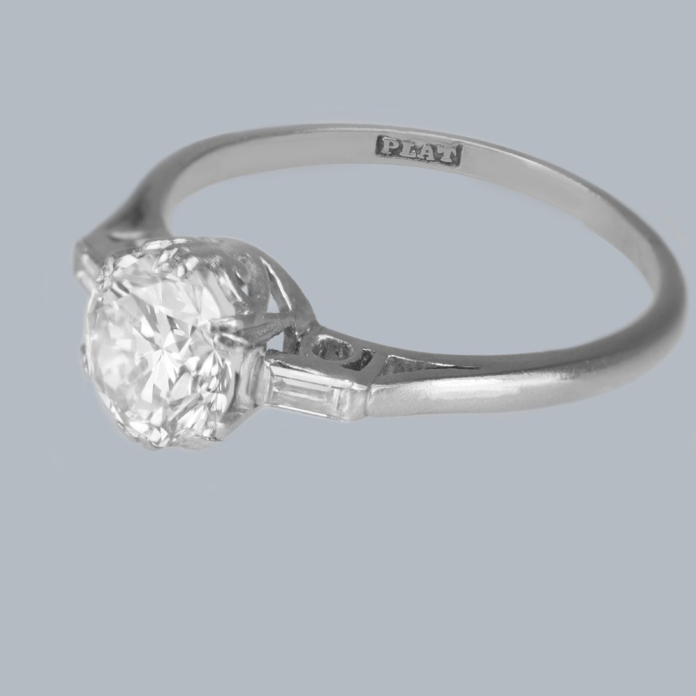 An Art Deco platinum solitaire ring featuring a round brilliant cut diamond flanked by stepped baguette cut shoulder stones. View X