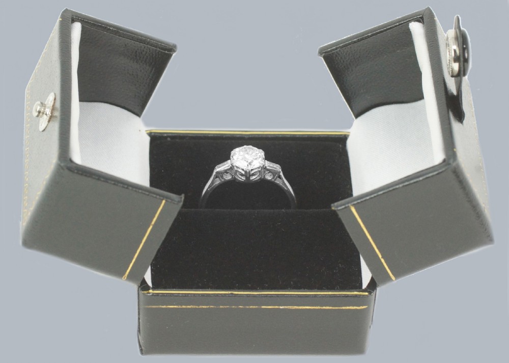 An Art Deco platinum solitaire ring featuring a round brilliant cut diamond flanked by stepped baguette cut shoulder stones. View XI