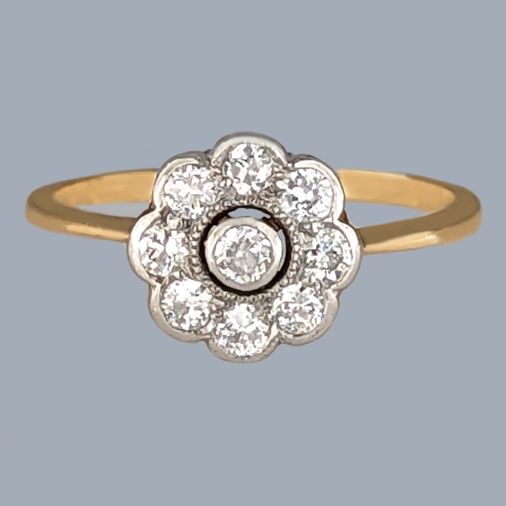 An Edwardian cluster ring in 18ct yellow gold and platinum featuring a central diamond surrounded by a floral halo of smaller diamonds.