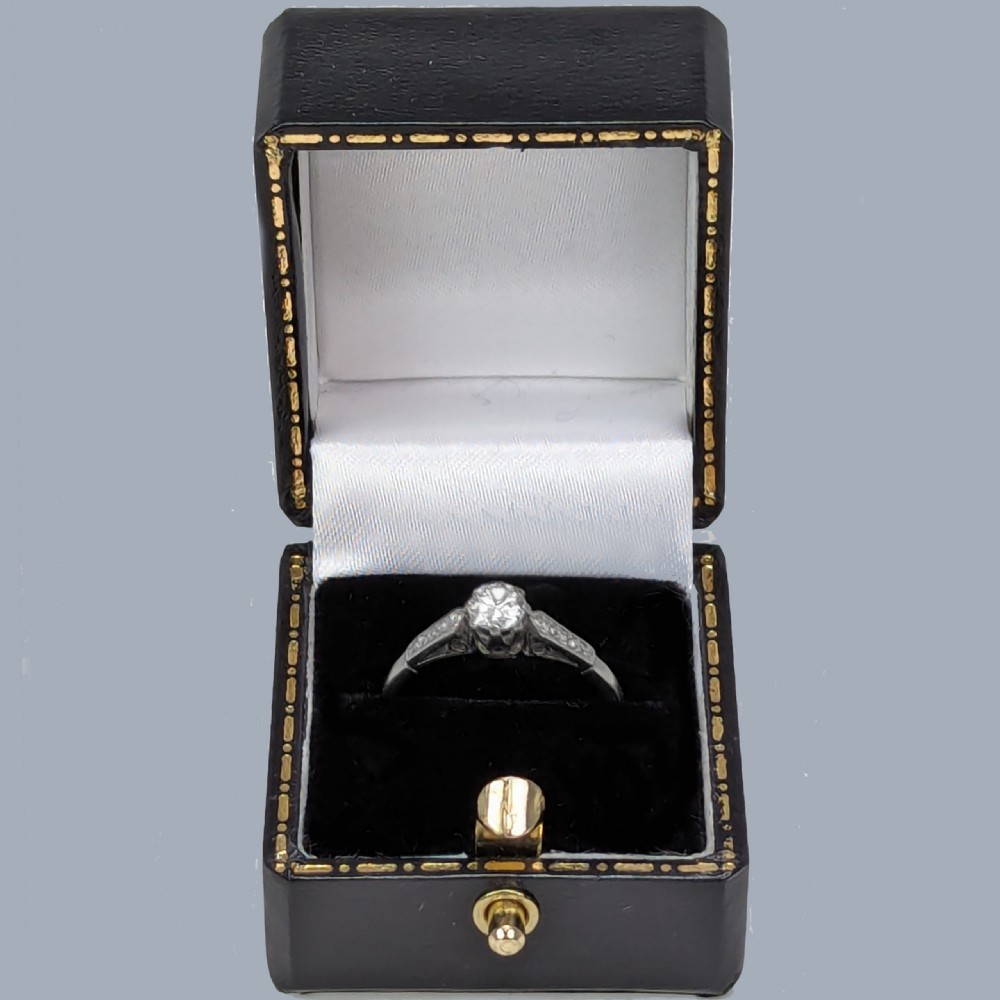 A vintage platinum solitaire ring featuring a round central diamond flanked by diamond-set shoulders. View VI