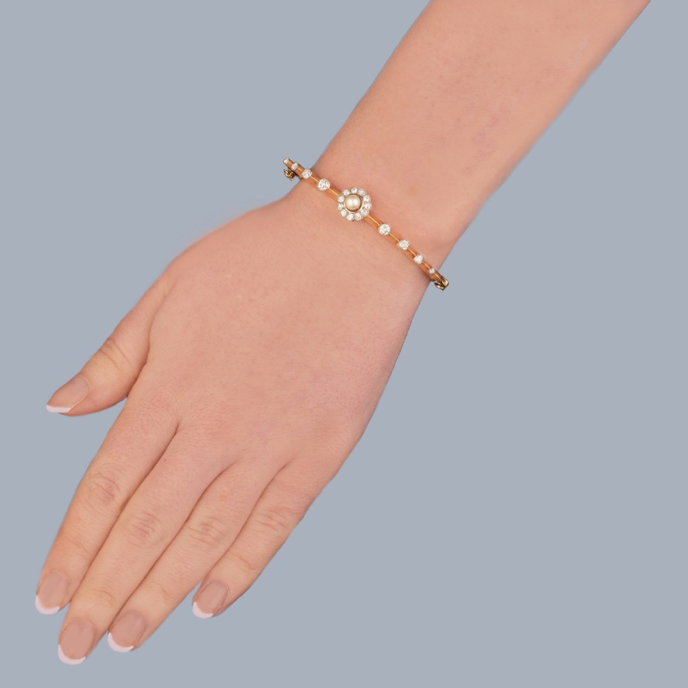 An antique Edwardian 18ct gold hinged bangle featuring a central diamond and pearl cluster motif flanked by graduated round-cut diamonds in platinum settings. View II