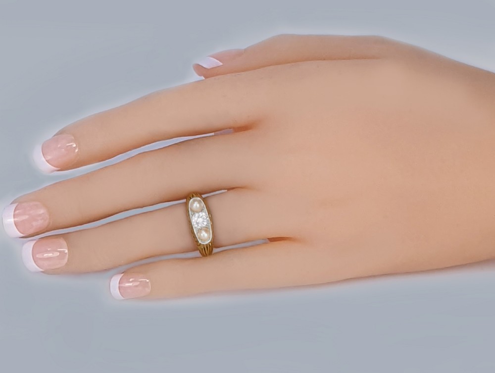 An Edwardian 18ct yellow gold ring featuring a central old cut diamond flanked by two pearls set within a white metal gallery. View III