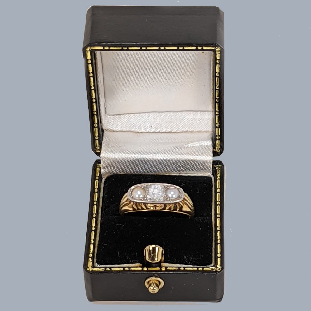 An Edwardian 18ct yellow gold ring featuring a central old cut diamond flanked by two pearls set within a white metal gallery. View X