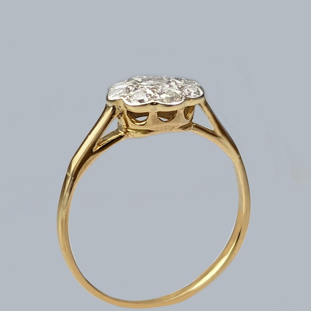 An 18ct yellow gold ring featuring a central diamond surrounded by a cluster of smaller round diamonds in a floral daisy pattern. View V