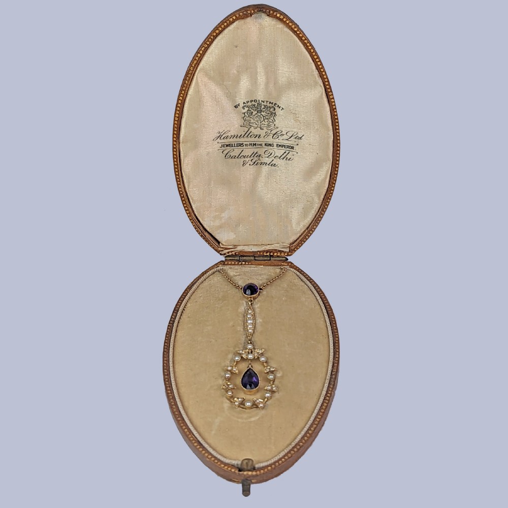A Victorian gold pendant necklace featuring a central teardrop amethyst suspended within a seed pearl foliate wreath, attached to a gold chain. View IV