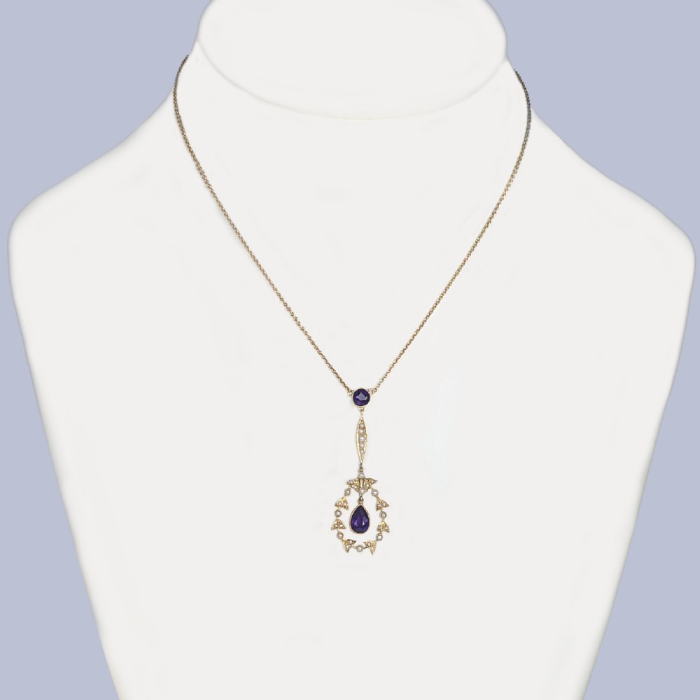 A Victorian gold pendant necklace featuring a central teardrop amethyst suspended within a seed pearl foliate wreath, attached to a gold chain. View V