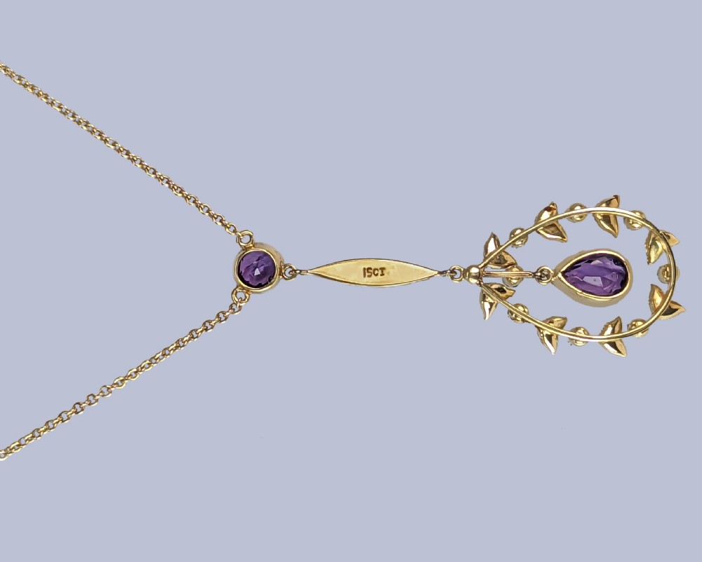 A Victorian gold pendant necklace featuring a central teardrop amethyst suspended within a seed pearl foliate wreath, attached to a gold chain. View VI