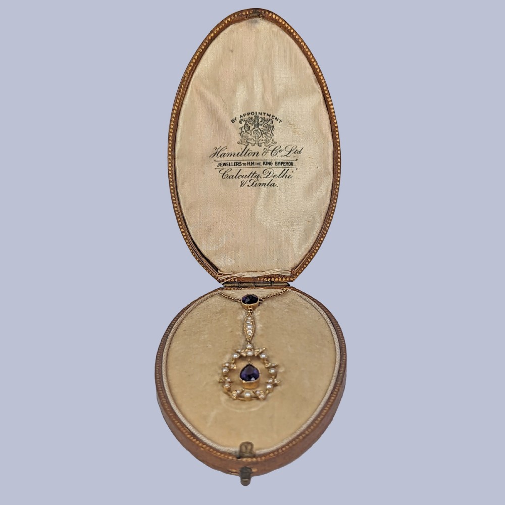 A Victorian gold pendant necklace featuring a central teardrop amethyst suspended within a seed pearl foliate wreath, attached to a gold chain. View IX