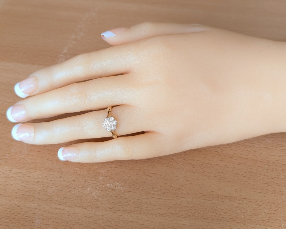 An antique 18ct yellow gold ring featuring a seven-stone diamond cluster set in a flower shape on split scrolled shoulders. View X
