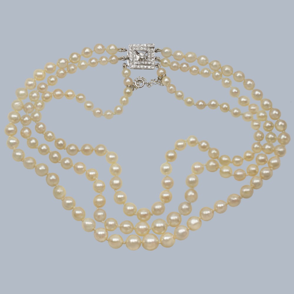 An Art Deco triple-strand cultured pearl necklace with a square geometric clasp set with brilliant diamonds.