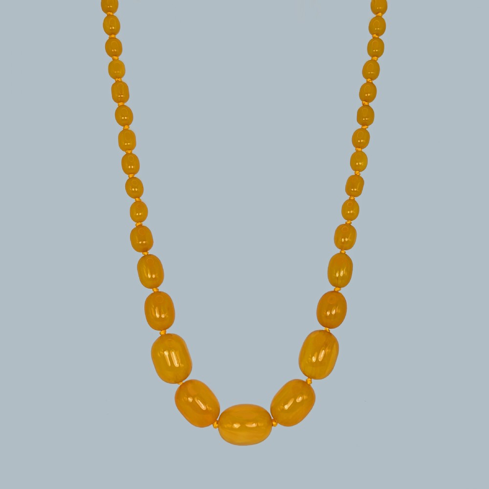 A continuous strand of opaque warm yellow graduated oval amber beads arranged symmetrically.