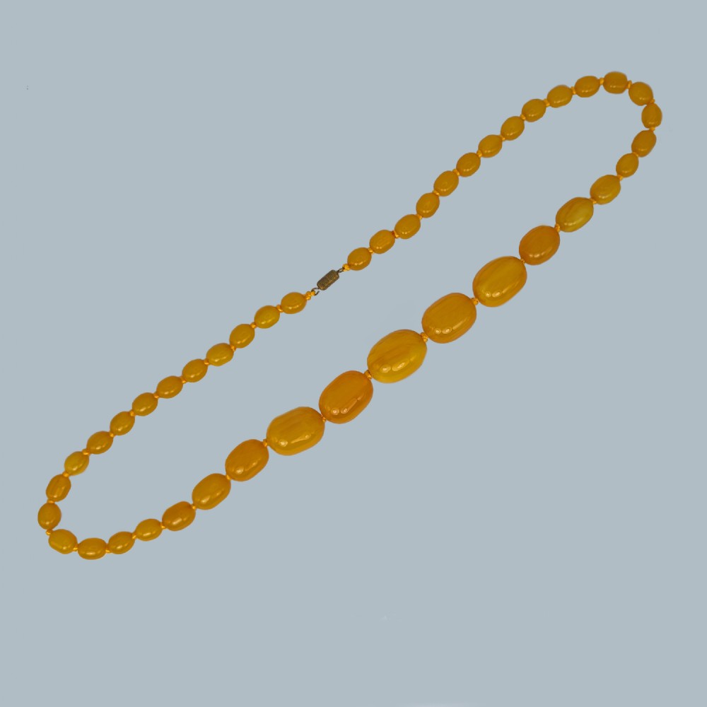 A continuous strand of opaque warm yellow graduated oval amber beads arranged symmetrically. View II