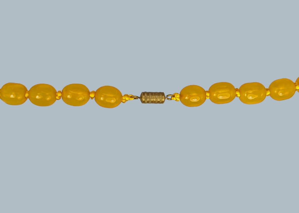A continuous strand of opaque warm yellow graduated oval amber beads arranged symmetrically. View III