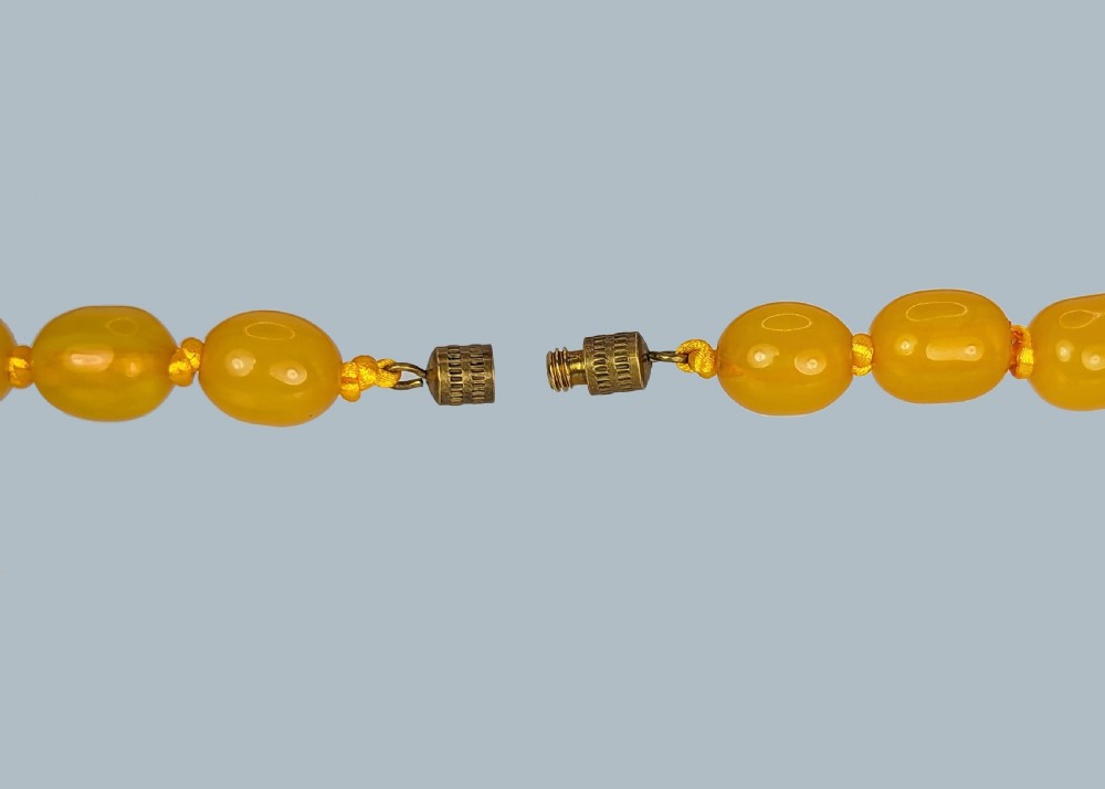 A continuous strand of opaque warm yellow graduated oval amber beads arranged symmetrically. View IV