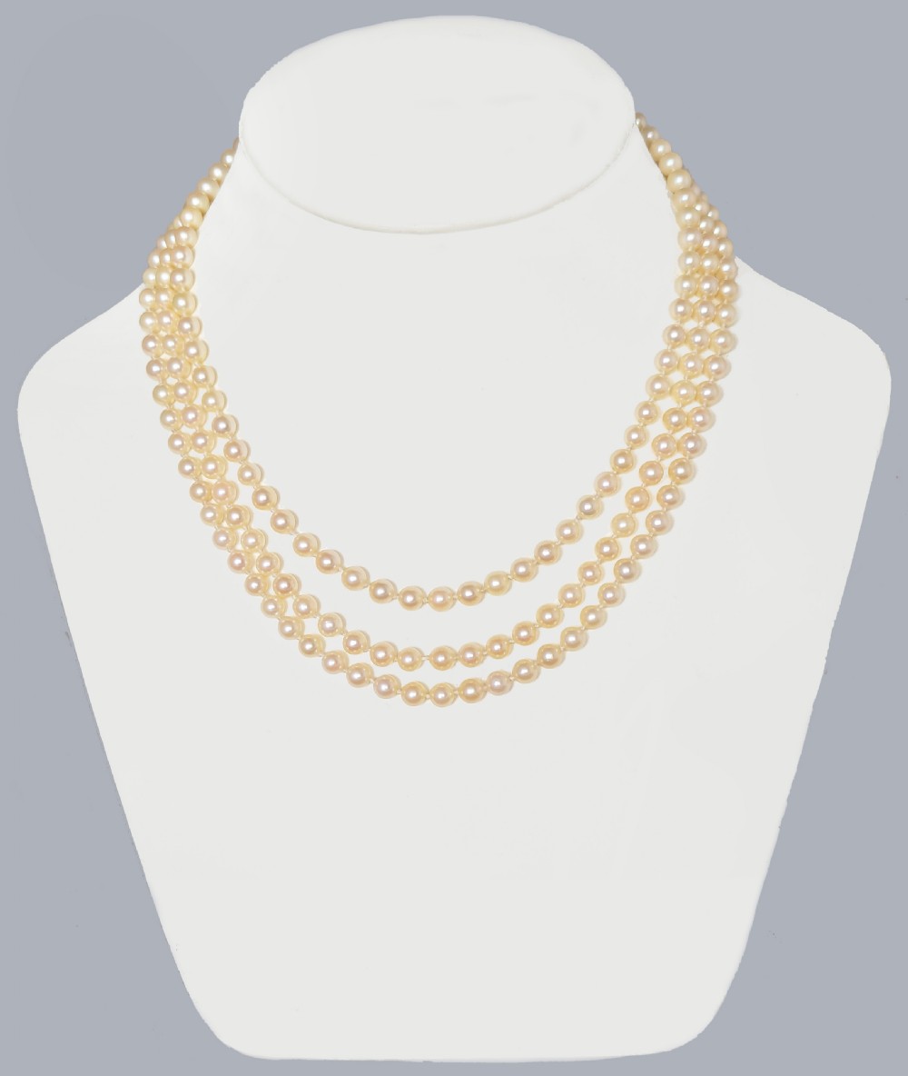 A triple strand cultured pearl necklace featuring cream pearls and a circular 9ct gold clasp inset with blue sapphires. View II