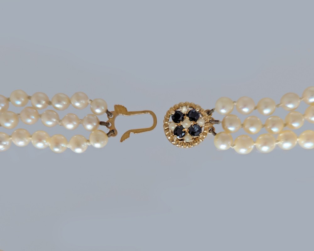 A triple strand cultured pearl necklace featuring cream pearls and a circular 9ct gold clasp inset with blue sapphires. View VI