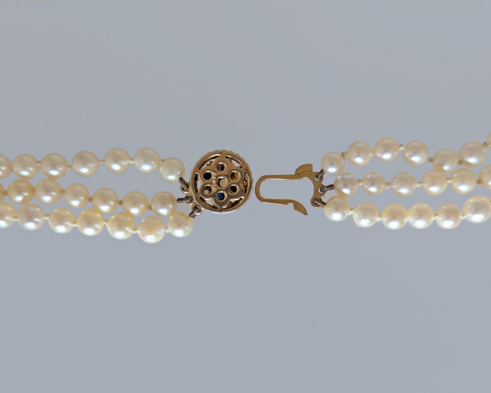 A triple strand cultured pearl necklace featuring cream pearls and a circular 9ct gold clasp inset with blue sapphires. View VII