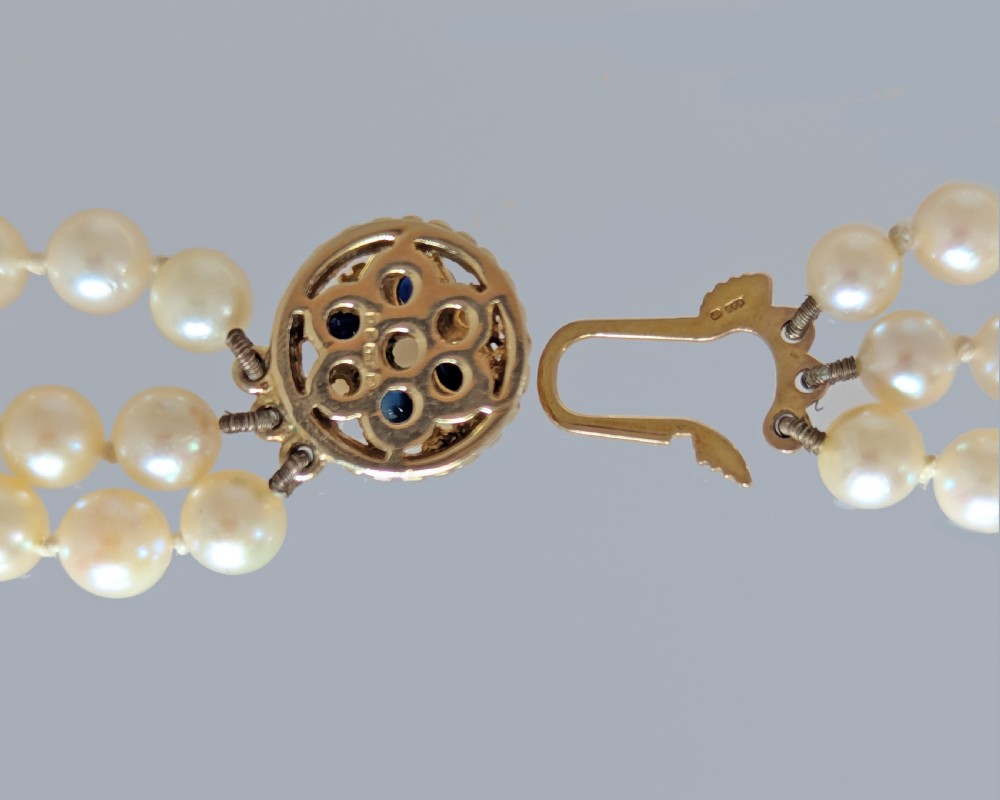A triple strand cultured pearl necklace featuring cream pearls and a circular 9ct gold clasp inset with blue sapphires. View VIII