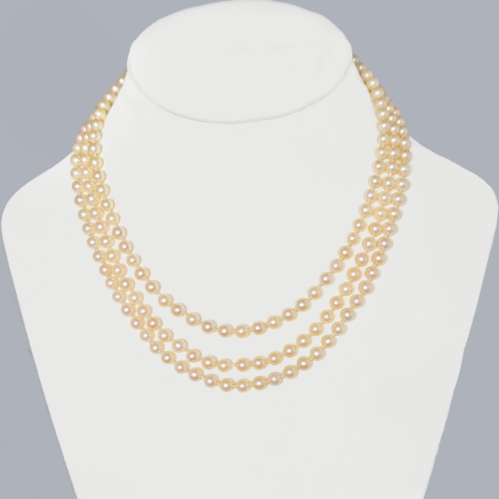 A triple strand cultured pearl necklace featuring cream pearls and a circular 9ct gold clasp inset with blue sapphires. View X