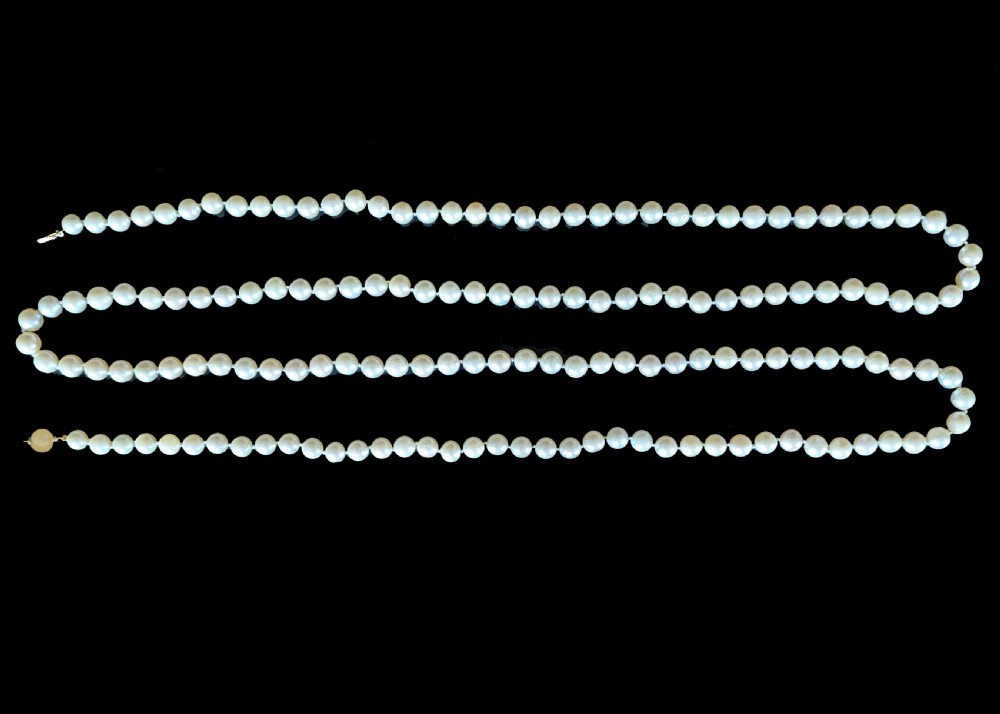 A long vintage cultured pearl sautoir necklace layered in multiple loops around a neck, featuring a small spherical gold clasp. View IV