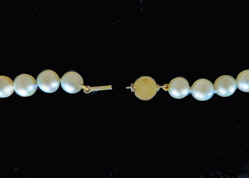 A long vintage cultured pearl sautoir necklace layered in multiple loops around a neck, featuring a small spherical gold clasp. View V