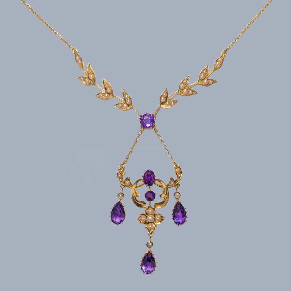 An Edwardian 15ct yellow gold necklace featuring foliate leaf motifs set with seed pearls and an openwork pendant with faceted purple amethysts.