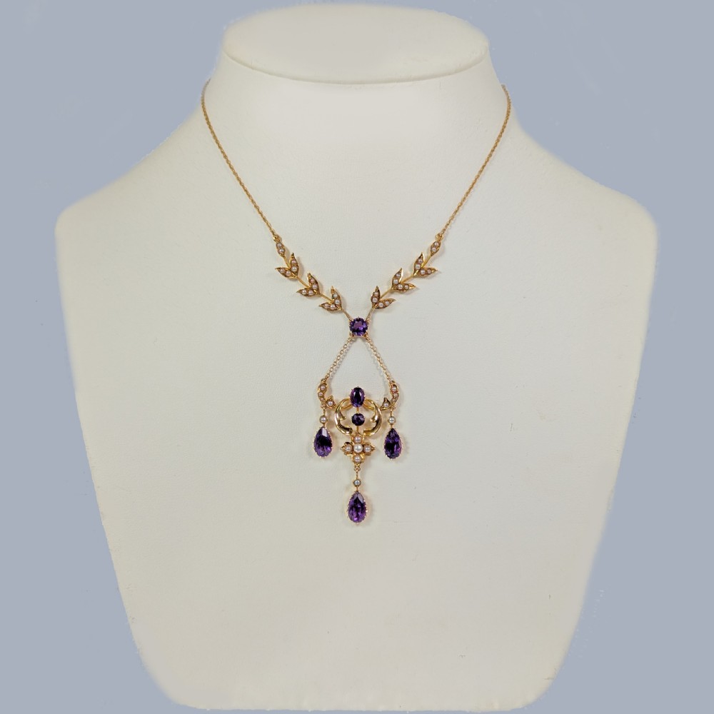 An Edwardian 15ct yellow gold necklace featuring foliate leaf motifs set with seed pearls and an openwork pendant with faceted purple amethysts. View V
