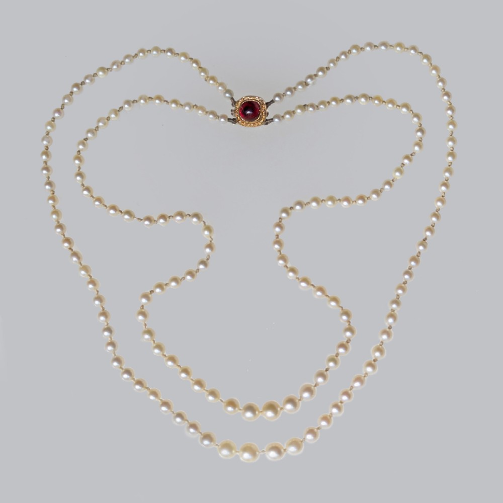 A 1950s double strand cultured pearl necklace with two rows of cream pearls linked by a circular 9ct gold clasp featuring a cabochon garnet.
