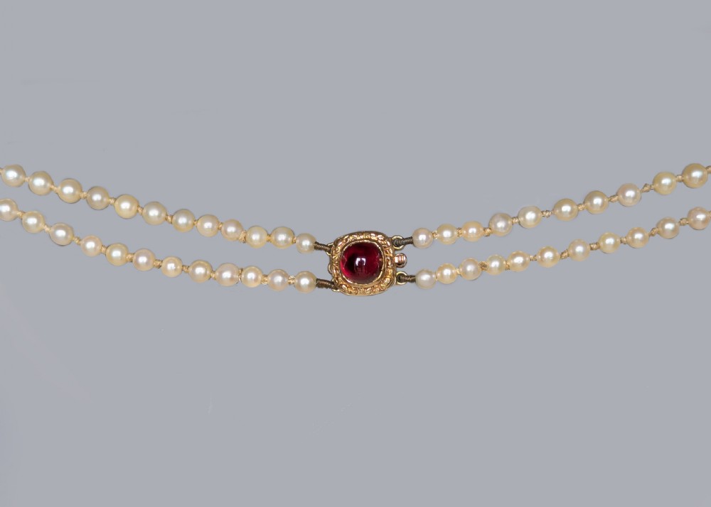 A 1950s double strand cultured pearl necklace with two rows of cream pearls linked by a circular 9ct gold clasp featuring a cabochon garnet. View III