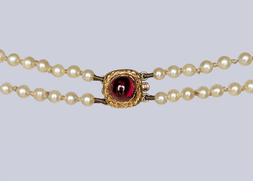 A 1950s double strand cultured pearl necklace with two rows of cream pearls linked by a circular 9ct gold clasp featuring a cabochon garnet. View IV