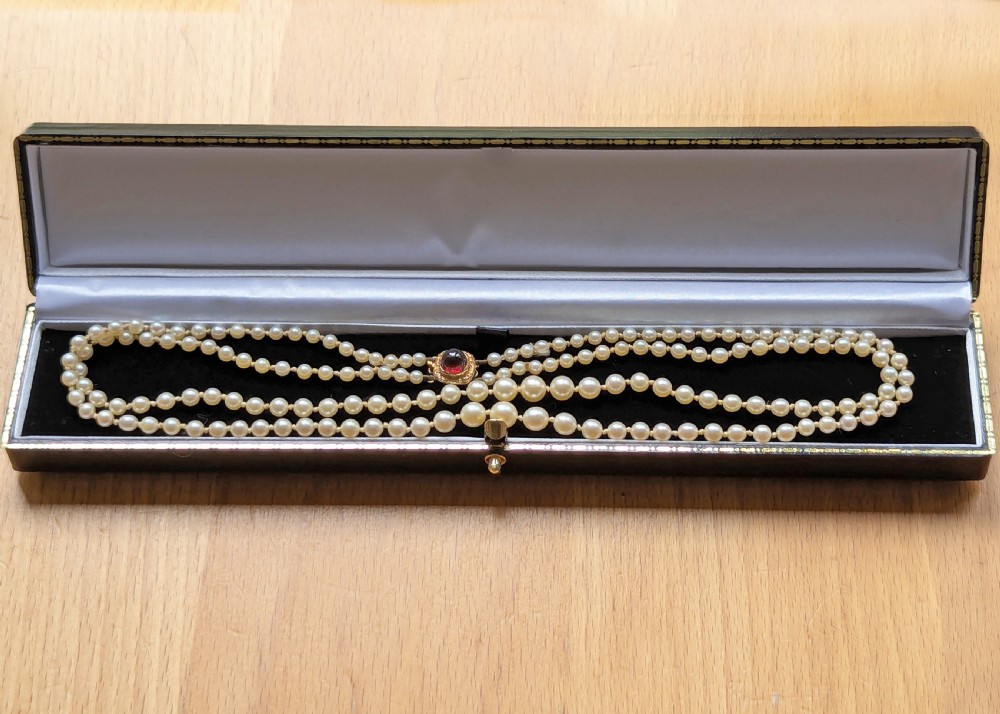 A 1950s double strand cultured pearl necklace with two rows of cream pearls linked by a circular 9ct gold clasp featuring a cabochon garnet. View X