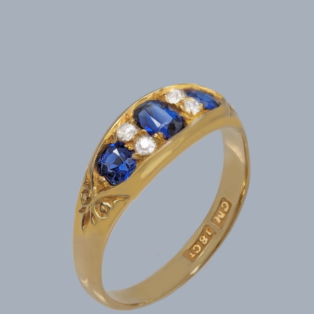 An 18ct yellow gold Victorian boat ring mounted with three central blue sapphires and four accent diamonds within a carved gallery. View III
