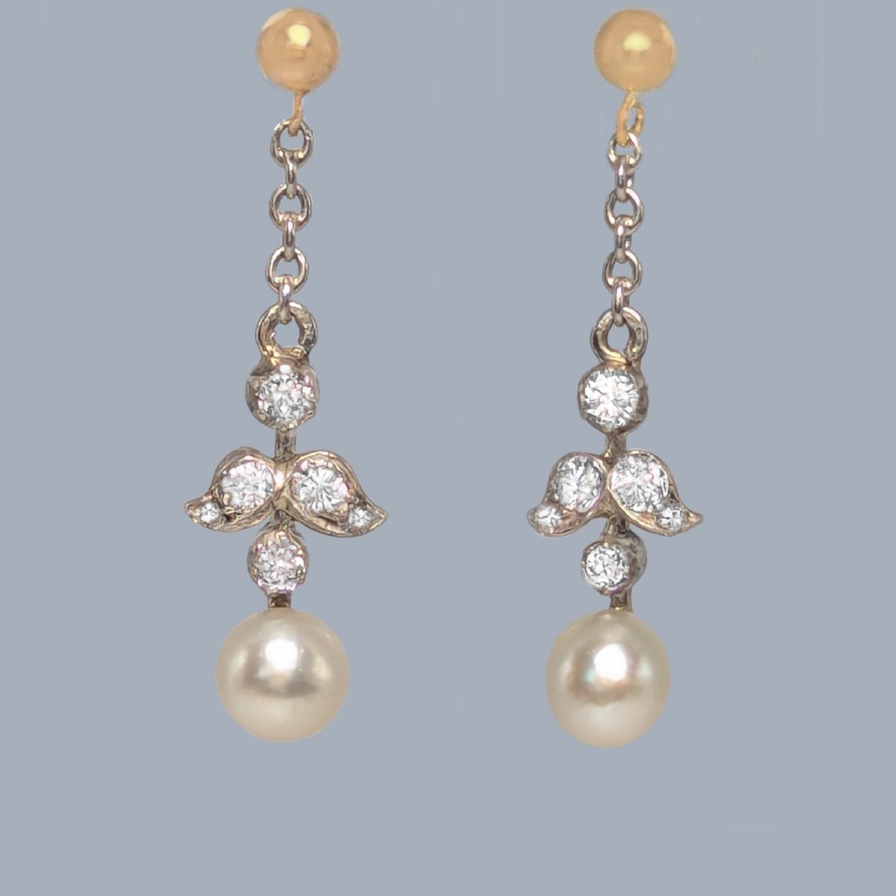 A pair of Edwardian drop earrings featuring gold studs connected by fine chain links to diamond-set foliate motifs and single white pearl drops.
