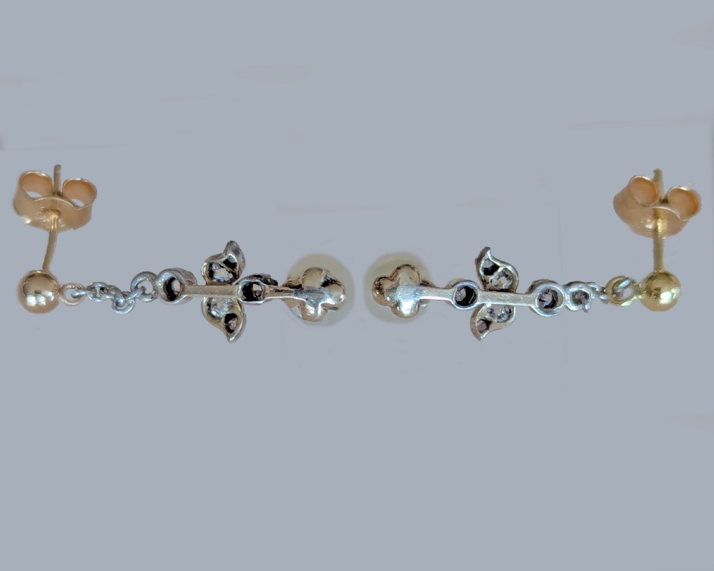 A pair of Edwardian drop earrings featuring gold studs connected by fine chain links to diamond-set foliate motifs and single white pearl drops. View VI