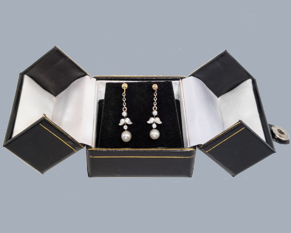 A pair of Edwardian drop earrings featuring gold studs connected by fine chain links to diamond-set foliate motifs and single white pearl drops. View VII