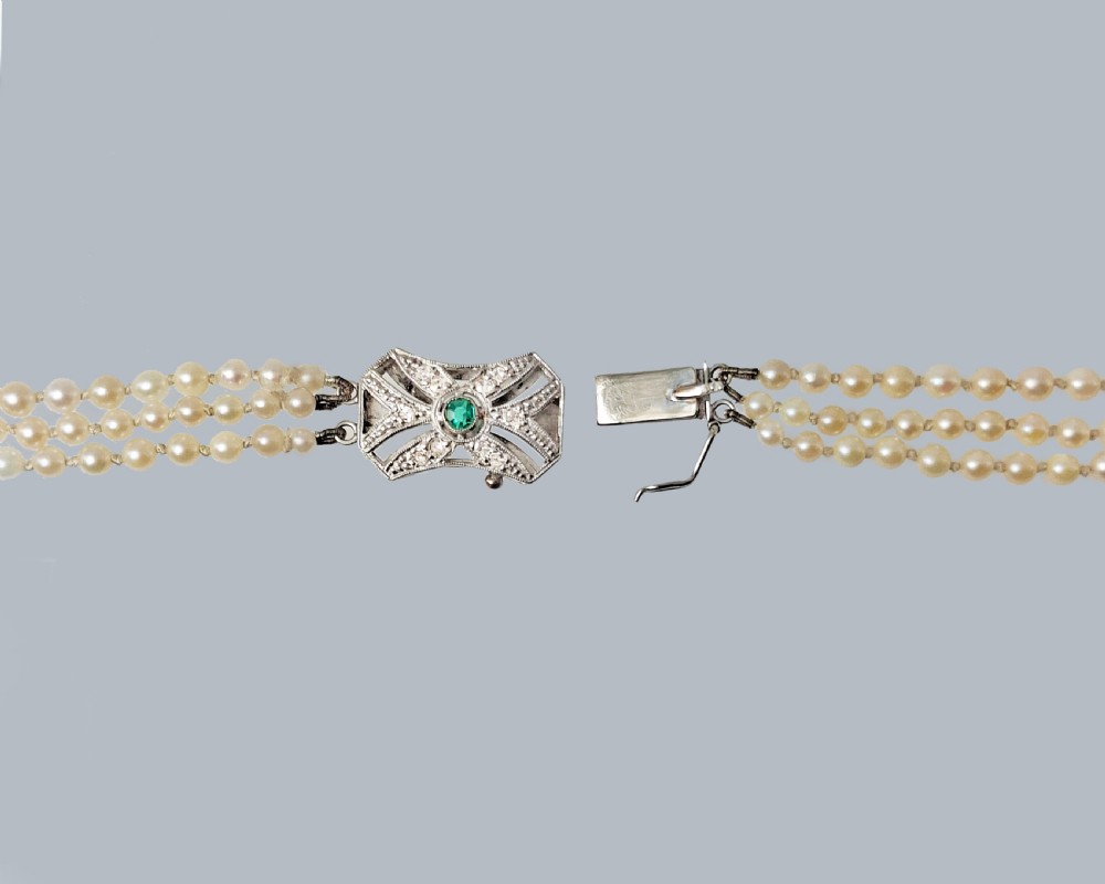 A 1950s three-strand pearl necklace featuring graduated pearls joined by a geometric clasp set with diamonds and a central green emerald. View III