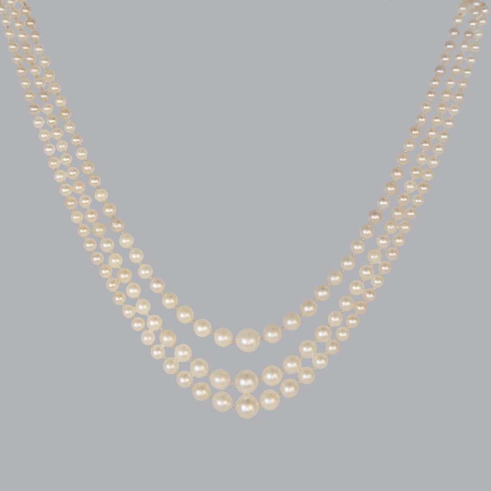 A 1950s three-strand pearl necklace featuring graduated pearls joined by a geometric clasp set with diamonds and a central green emerald. View VI