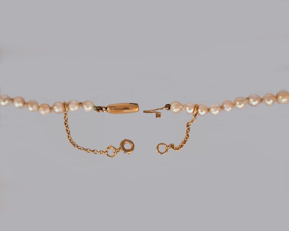 A single strand of graduated cream white cultured pearls with a yellow gold barrel clasp displayed on a beige neck bust. View IV