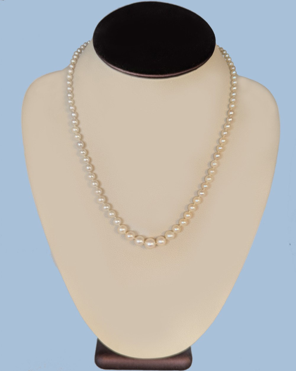 A single strand of graduated cream white cultured pearls with a yellow gold barrel clasp displayed on a beige neck bust. View VI