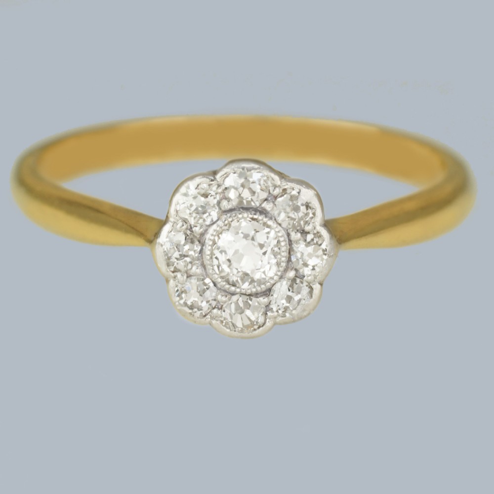 An Edwardian diamond cluster ring featuring a central old European cut diamond surrounded by eight smaller diamonds set in platinum on a yellow gold band.