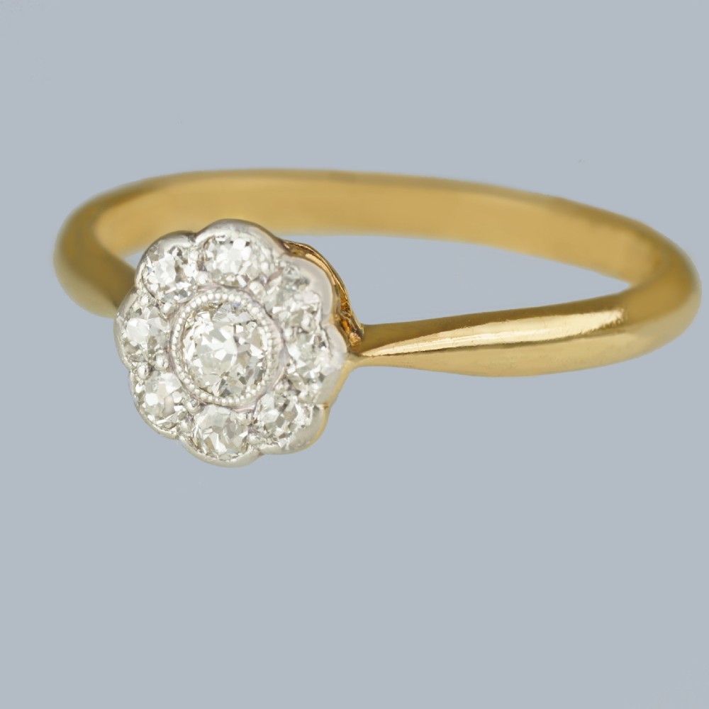 An Edwardian diamond cluster ring featuring a central old European cut diamond surrounded by eight smaller diamonds set in platinum on a yellow gold band. View II