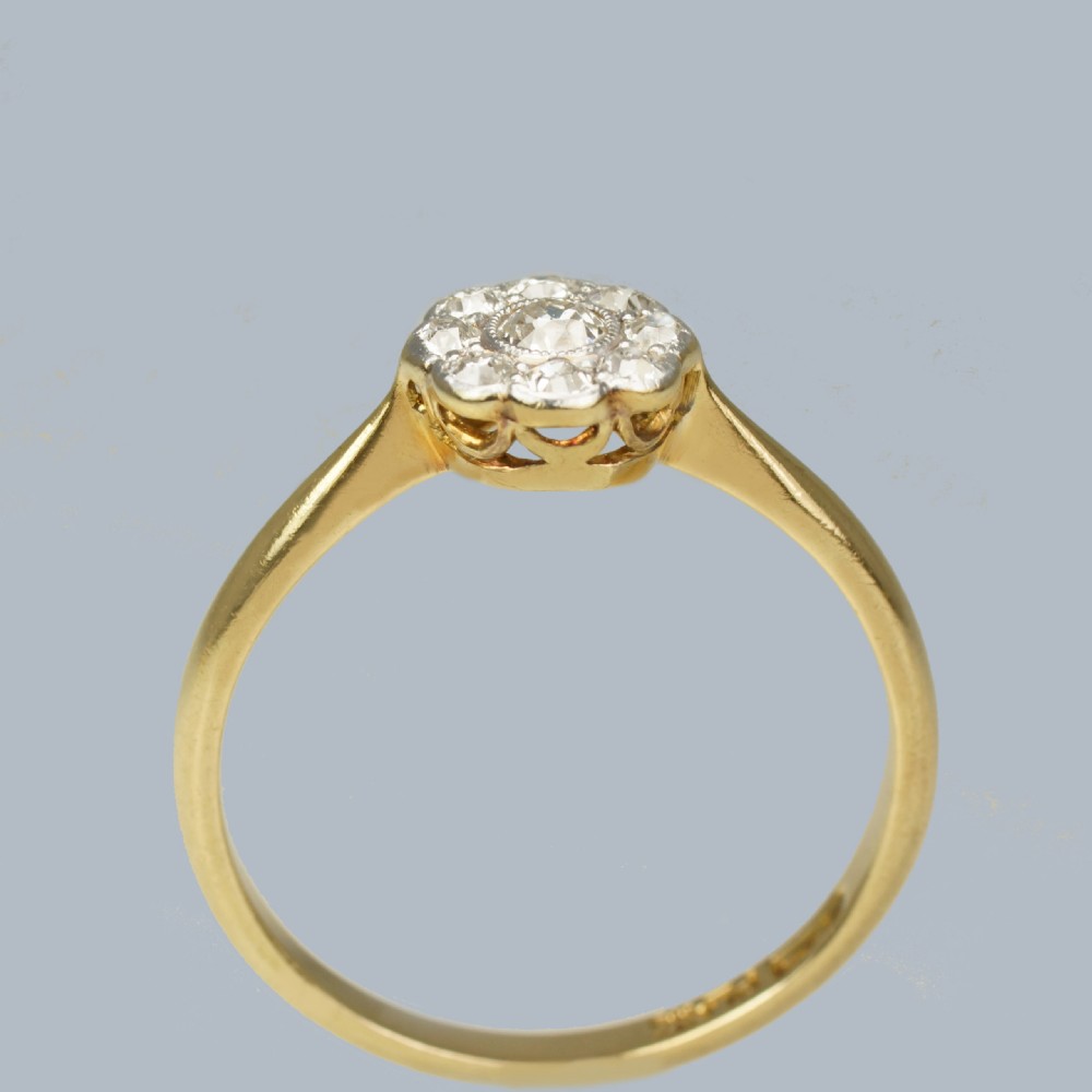 An Edwardian diamond cluster ring featuring a central old European cut diamond surrounded by eight smaller diamonds set in platinum on a yellow gold band. View III