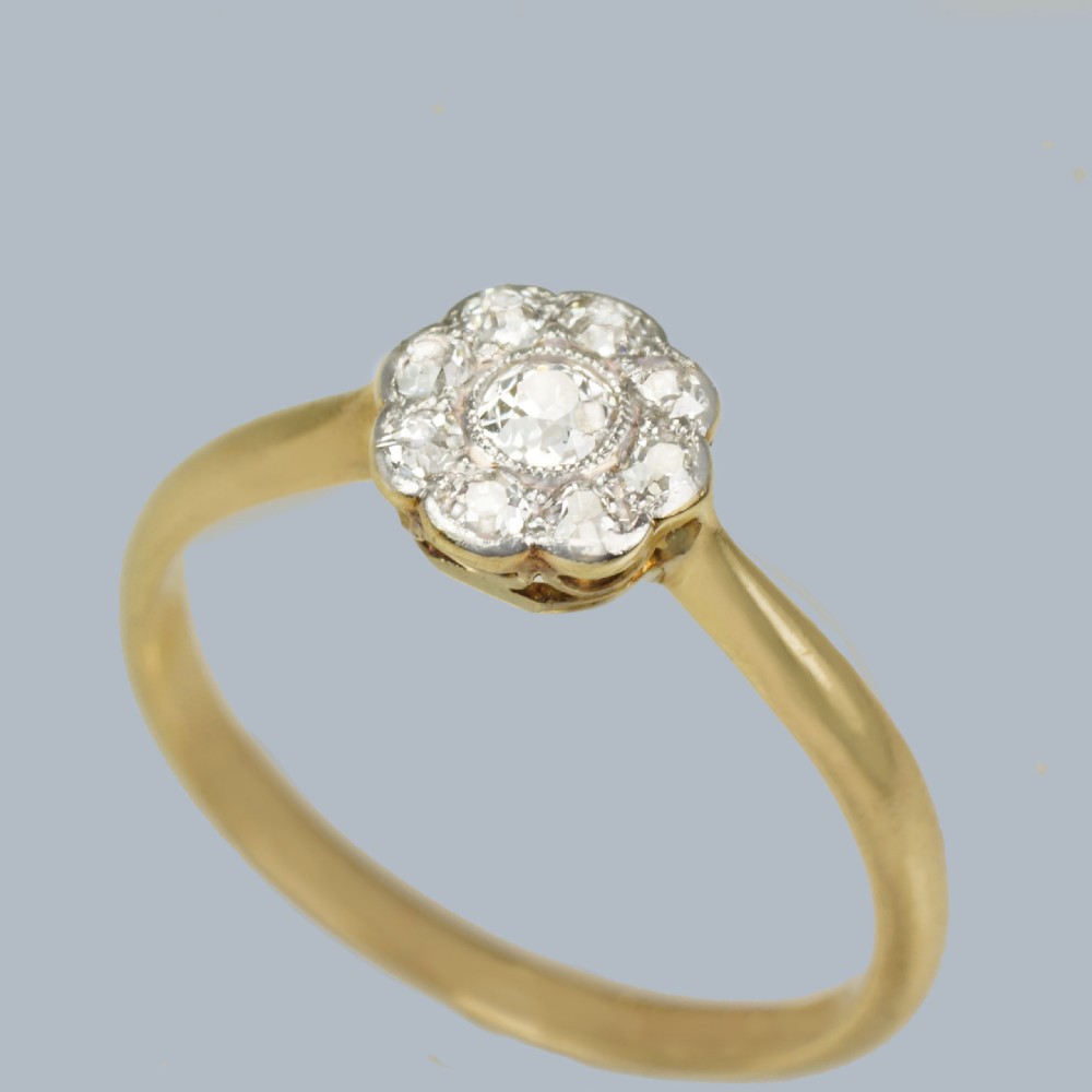 An Edwardian diamond cluster ring featuring a central old European cut diamond surrounded by eight smaller diamonds set in platinum on a yellow gold band. View IV