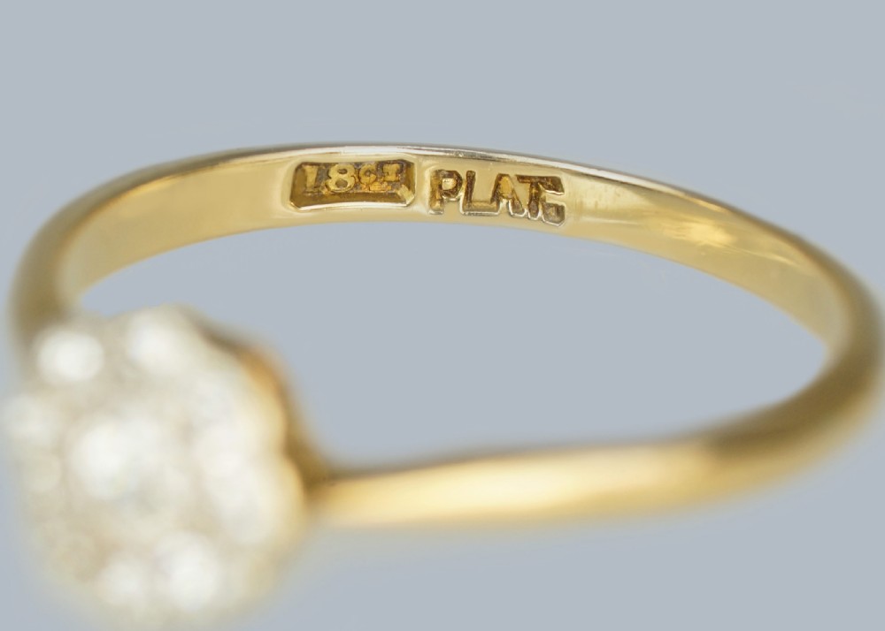An Edwardian diamond cluster ring featuring a central old European cut diamond surrounded by eight smaller diamonds set in platinum on a yellow gold band. View V