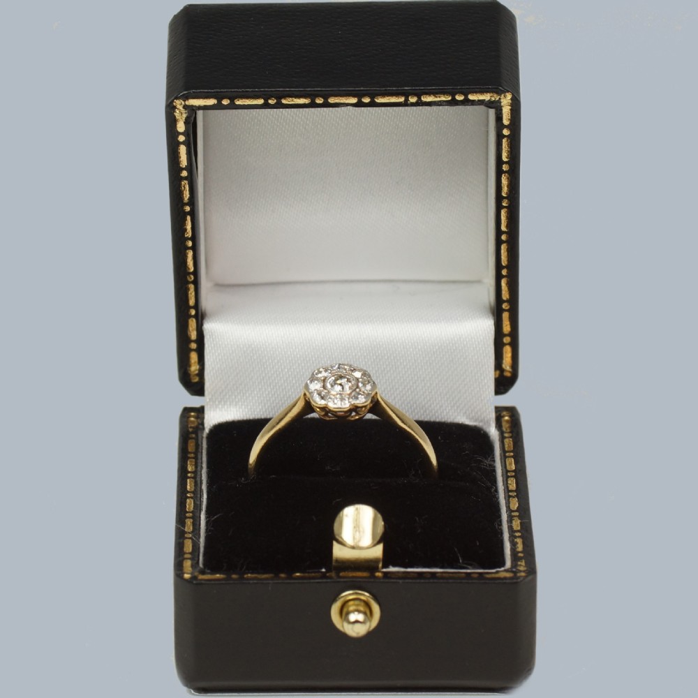 An Edwardian diamond cluster ring featuring a central old European cut diamond surrounded by eight smaller diamonds set in platinum on a yellow gold band. View VI