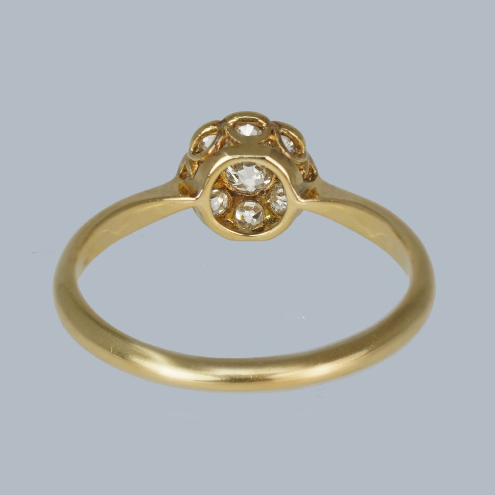 An Edwardian diamond cluster ring featuring a central old European cut diamond surrounded by eight smaller diamonds set in platinum on a yellow gold band. View VII