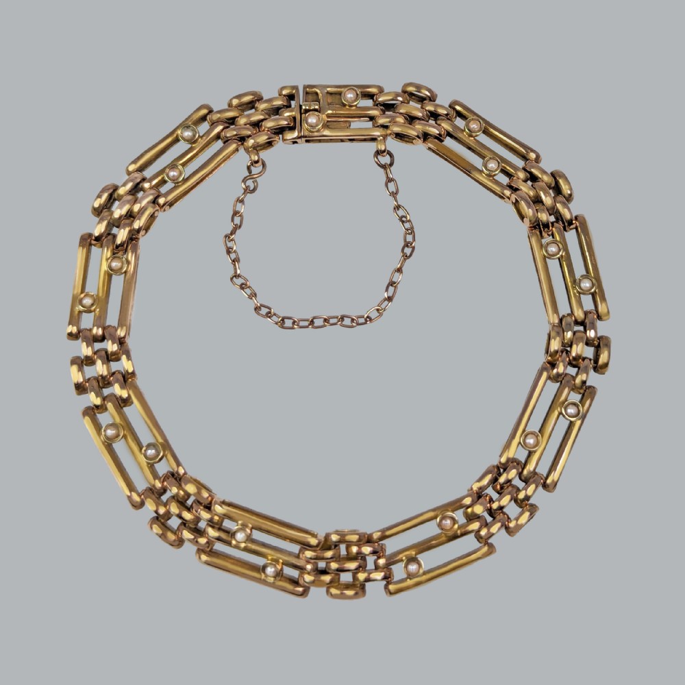 A circular Victorian 15ct yellow gold gate link bracelet set with split pearls and featuring a safety chain.