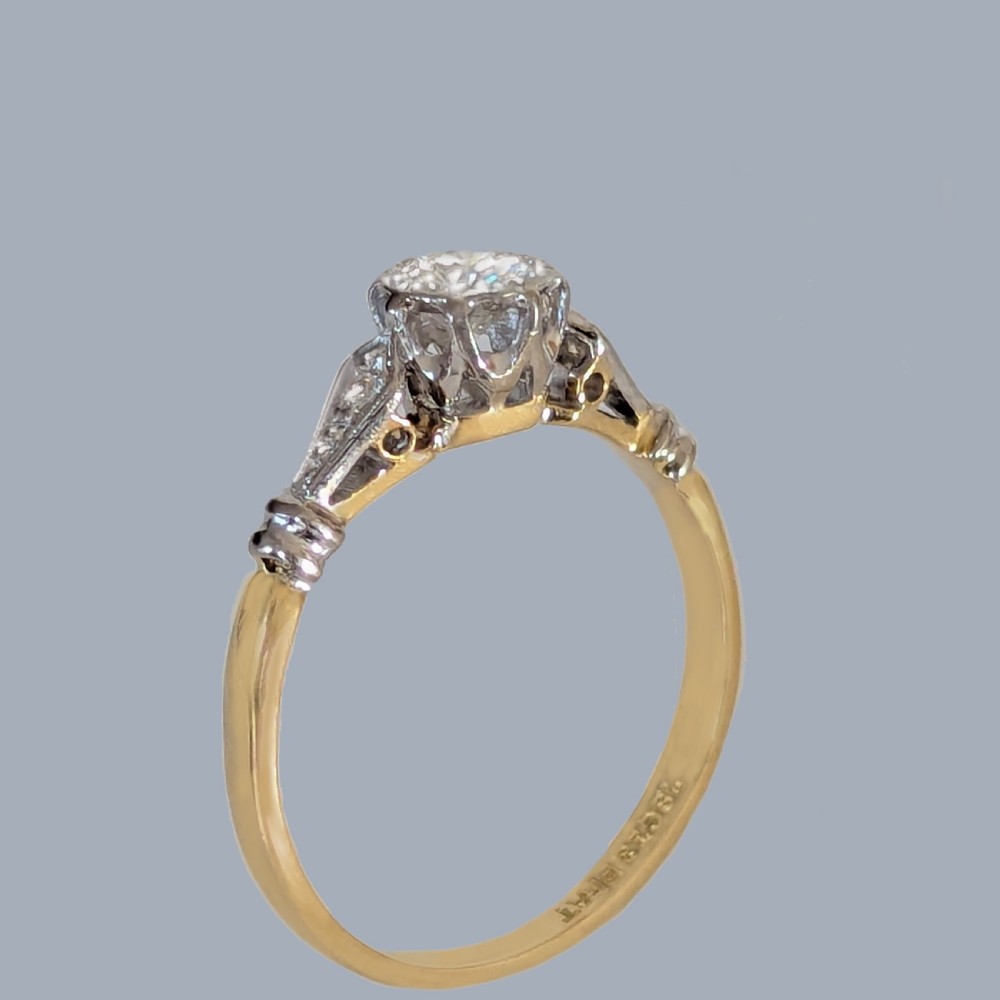 An antique 1920s diamond solitaire ring with a round cut central diamond set in platinum with geometric shoulders on an 18ct yellow gold band. View VI