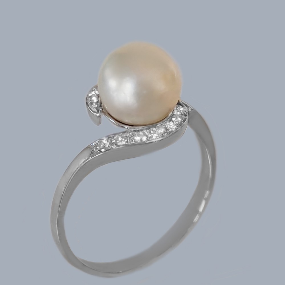 A 1950s 18ct white gold bypass ring featuring a central cream pearl enveloped by a swirling band set with small round diamonds. View VI