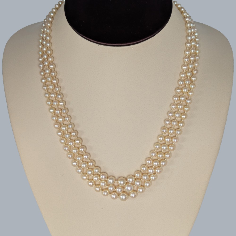 A 1950s triple strand pearl necklace featuring graduated cream pearls and a geometric diamond-set clasp with a safety chain. View IV